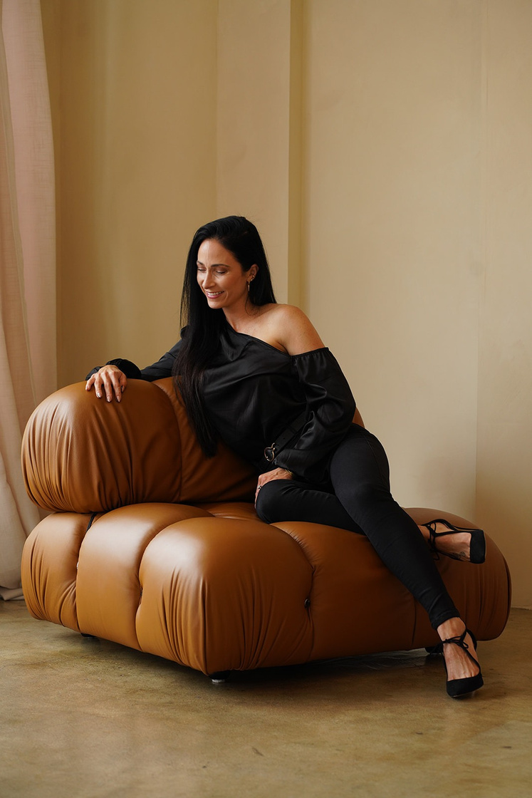 A woman smiling and sitting on a brown leather couch